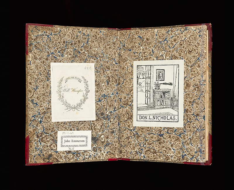 Patterned endpapers of an old book with three bookplates pasted onto them – two on the left, one on the right. One on the left has the text 'William Hamper' inside a decorative oval border. The other on the left reads 'John Emmerson' inside a simple rectangular border. The bookplate on the right is much more decorative: it reads 'Don L. Nicholas' and above the text there is an engraving of an interior scene featuring a bookshelf, a paitning and a gun.